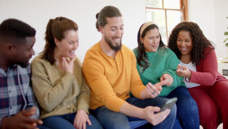 Happy-diverse-male-and-female-friends-relaxing-at-home-together-talking-and-looking-at-smartphone