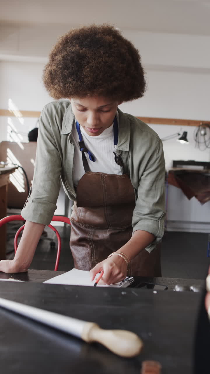 Vertical video of biracial female worker drawing design of jewellery in workshop in slow motion