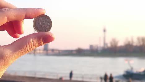 woman finger holding a 1 euro coin against the backdrop in front of the city of dusseldorf