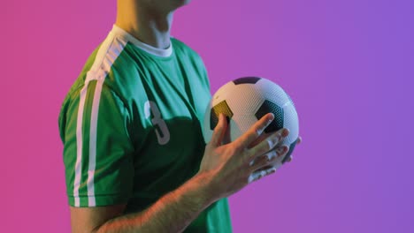 Caucasian-male-soccer-player-with-football-over-neon-pink-lighting