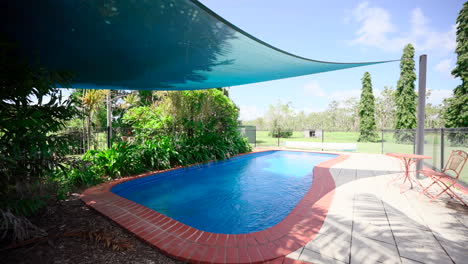 relaxing and calming large outdoor pool area with shade cloth covering cool water by tropical garden. exterior of home house for real estate property.