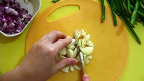 overhead or flatlay steady video shot of a person chopping garlic with a knife on a chopping board