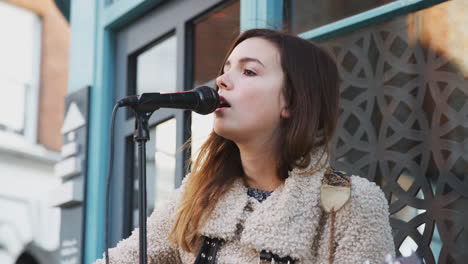 músico femenino tocando la guitarra acústica y cantando al aire libre en la calle