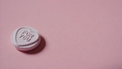 Hand-Picking-Up-Heart-Candy-With-Romantic-Message-For-You-On-Pink-Background