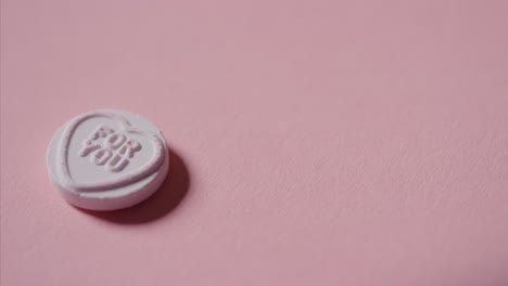 mano recogiendo caramelos de corazón con un mensaje romántico para ti sobre fondo rosa