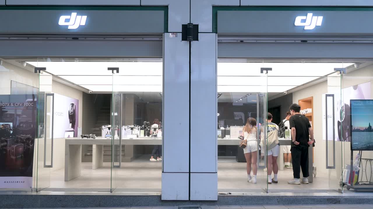Shoppers check out DJI’s drones and products inside the company’s flagship Hong Kong store, with a steady flow of pedestrians walking by in the evening.