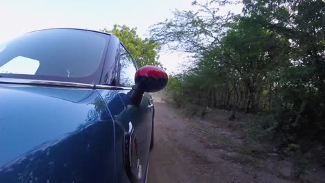 blue hatchback car moving on a dusty road, with red rear view mirror at high speed