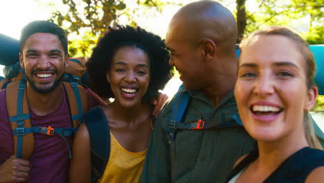 group of friends with backpacks posing for selfie on mobile phone on vacation hiking in countryside