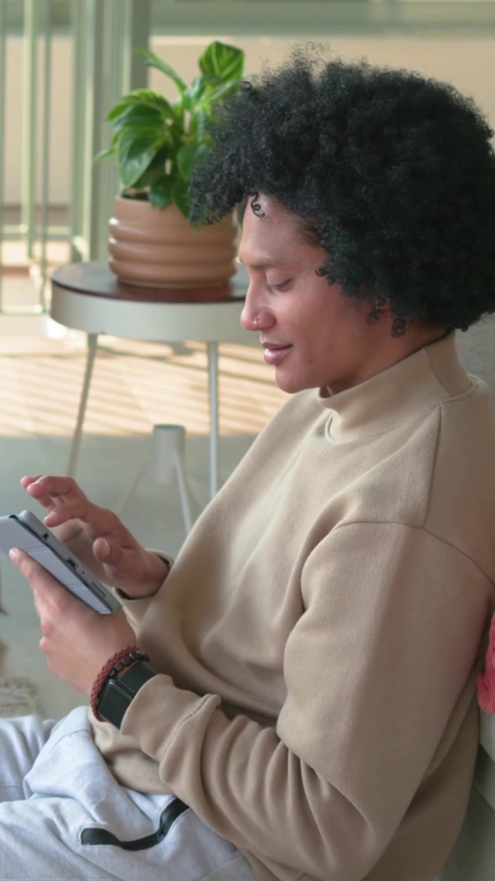 Vertical video: Picking up phone man in beige top tapping screen on sofa, browsing content, watch