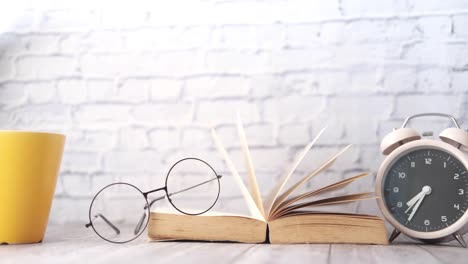 open book, glasses, and alarm clock on a wooden table