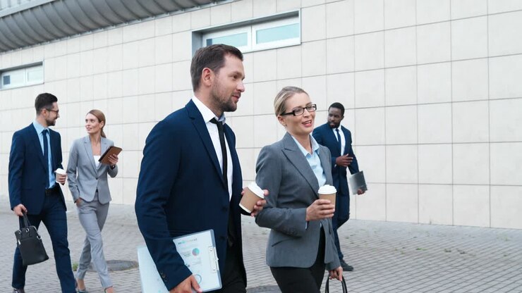 Caucasian couple of happy businessman and businesswoman walking down the street in the morning, talking and holding coffee to go