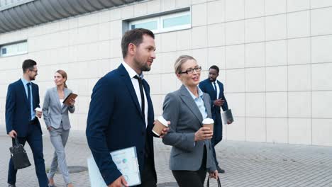 caucasian couple of happy businessman and businesswoman walking down the street in the morning, talking and holding coffee to go