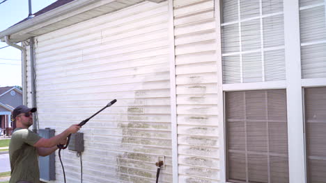 homeowner pressure washing side of house on summer day