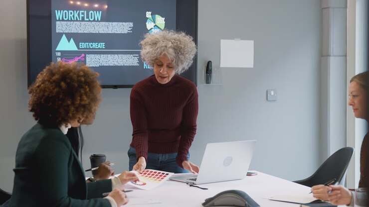 Donna d'affari matura che conduce una riunione creativa con donne che collaborano attorno a un tavolo in un ufficio moderno.