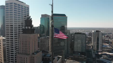 aerial-footage-of-America's-flag,-heading-backwards,-downtown-Minneapolis-in-the-background