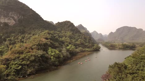 Scenic flight above lush hills and river filled with traditional boats, capturing the serene beauty of an untouched tropical valley landscape.