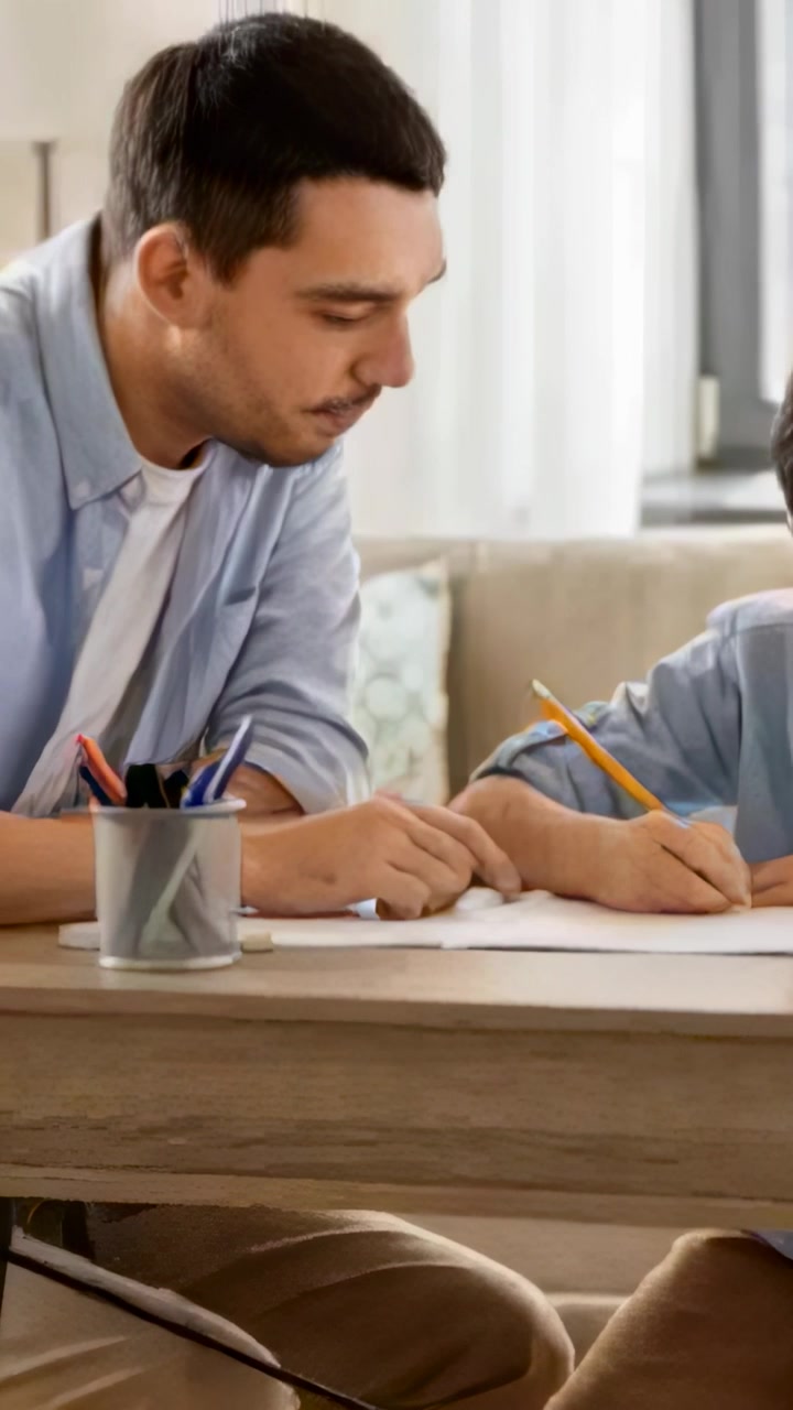 Video verticale: Notando un bambino che scrive, uomo appoggiato a casa che indica e guida una matita gialla per aiutare.