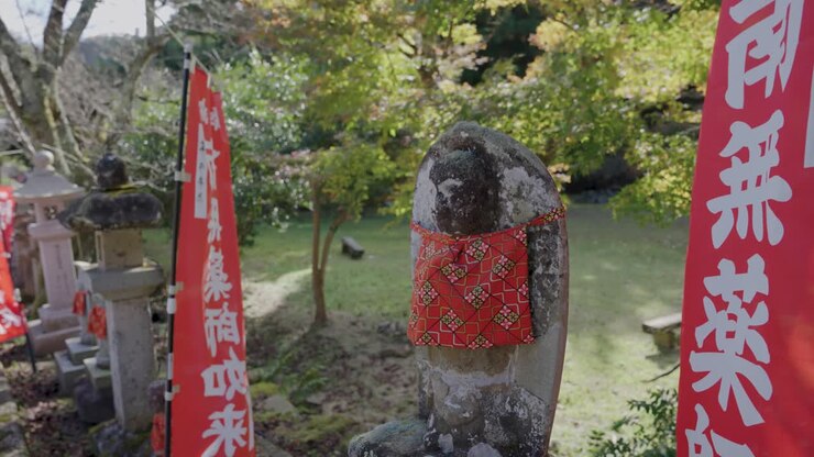 Statua di Jizo con sciarpa rossa in un tempio a Kinosaki Onsen, Giappone, in autunno sereno