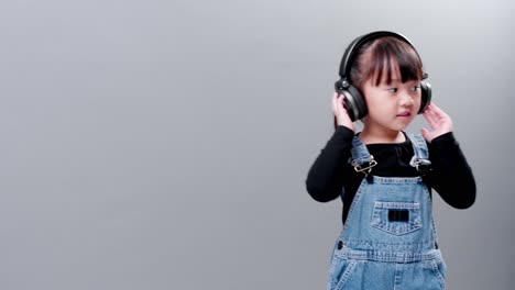 Child-listening-to-music-with-headset-wearing-jeans-on-gray-background-in-studio