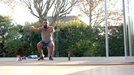 focused african american man doing squats on mat with tablet in garden, slow motion