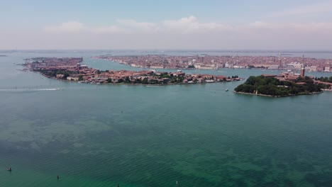 Venice-from-drone,-high-altitude-cinematic-orbit-shot-of-Venetian-islands-and-canals,-boats-speeding-in-the-foreground