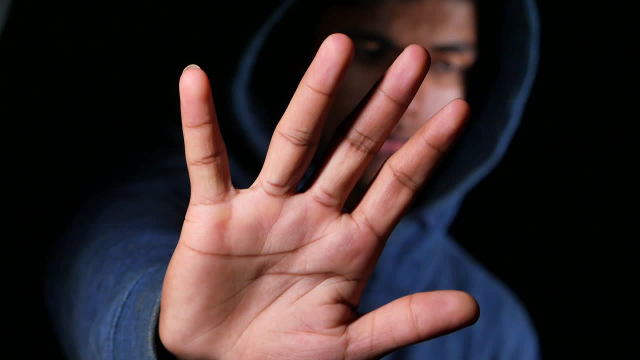 후디를 입은 신비한 남자가 멈추는 몸짓을 합니다.