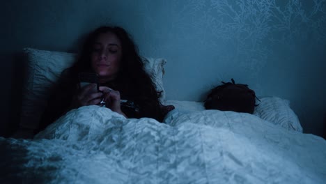 mujer se desplaza a través de su teléfono mientras estaba sentada en la cama por la noche
