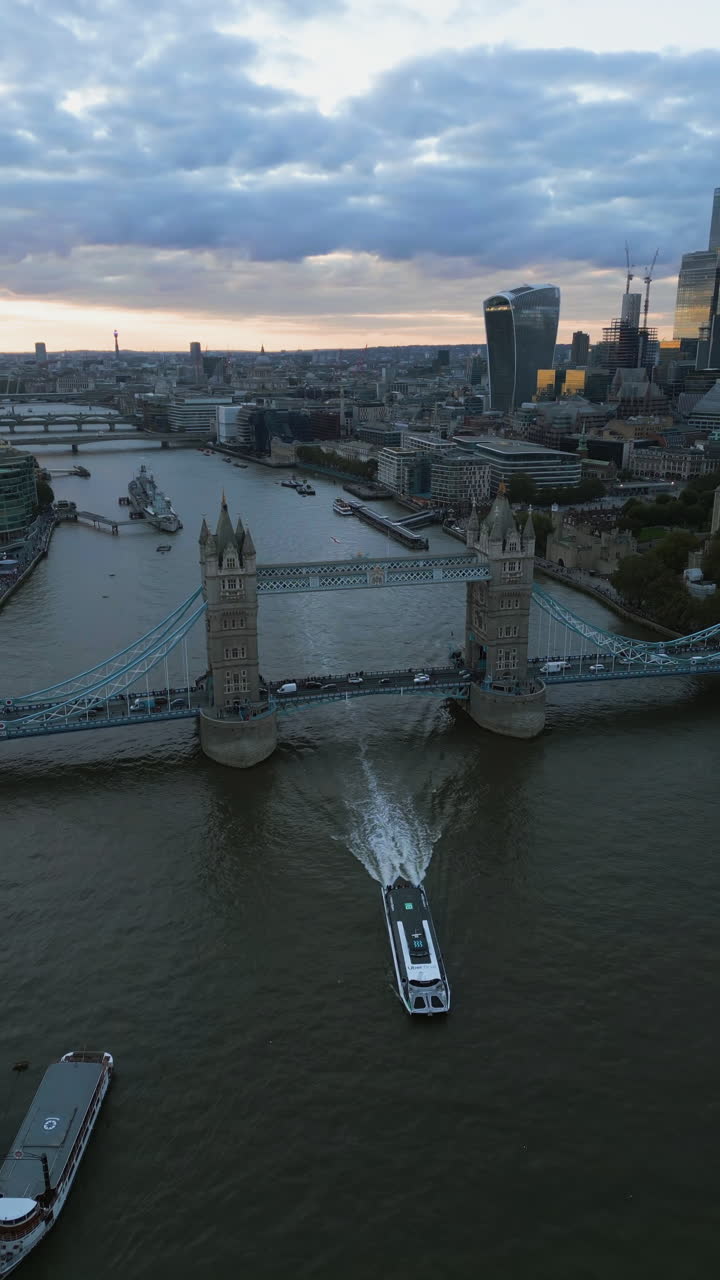Vertical drone shot of a riverboats passing the Tower bridge, sunset in London