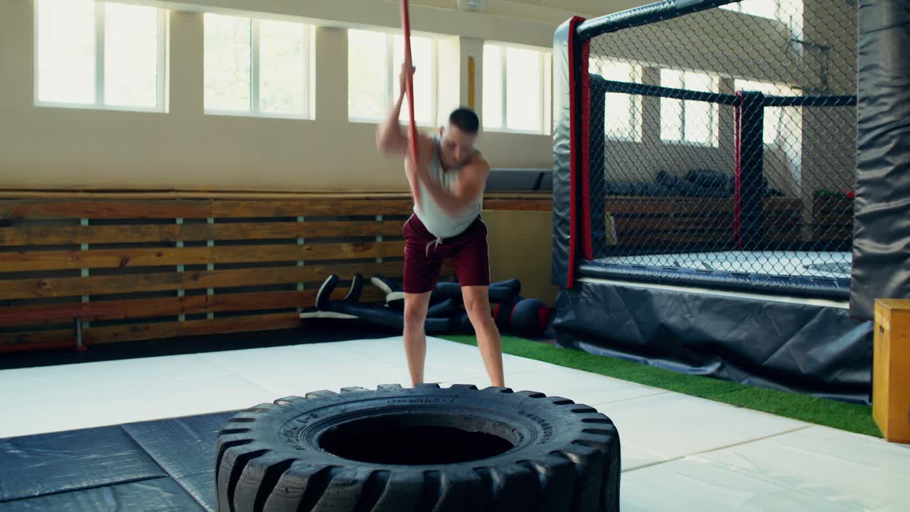 ジムでハンマーとタイヤを使って運動する男性