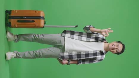 full body of asian male traveler with luggage and passport smiling and showing okay gesture while standing in the green screen background studio