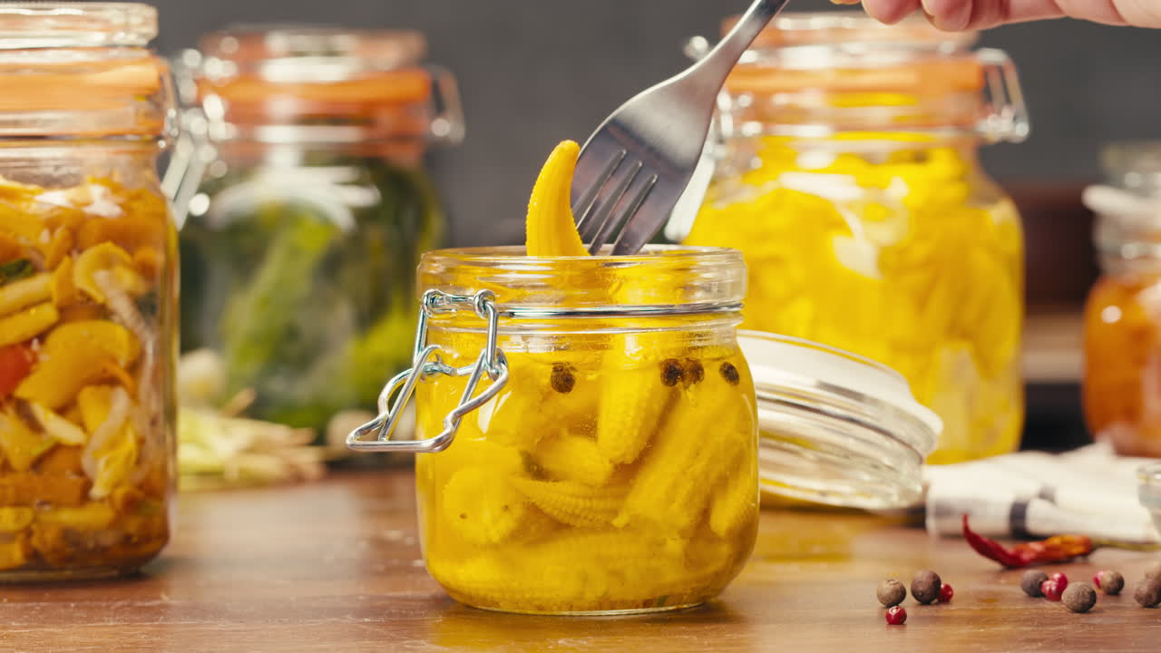 Fermented food in glass cans on table close-up. Preservation of vegetables in glass jars. Fermentation preserved mini corns, kimchi, cucumbers, mushrooms with spices.