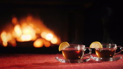 two cups with tea stand on a table on a black background where you can see the fire in the fireplace