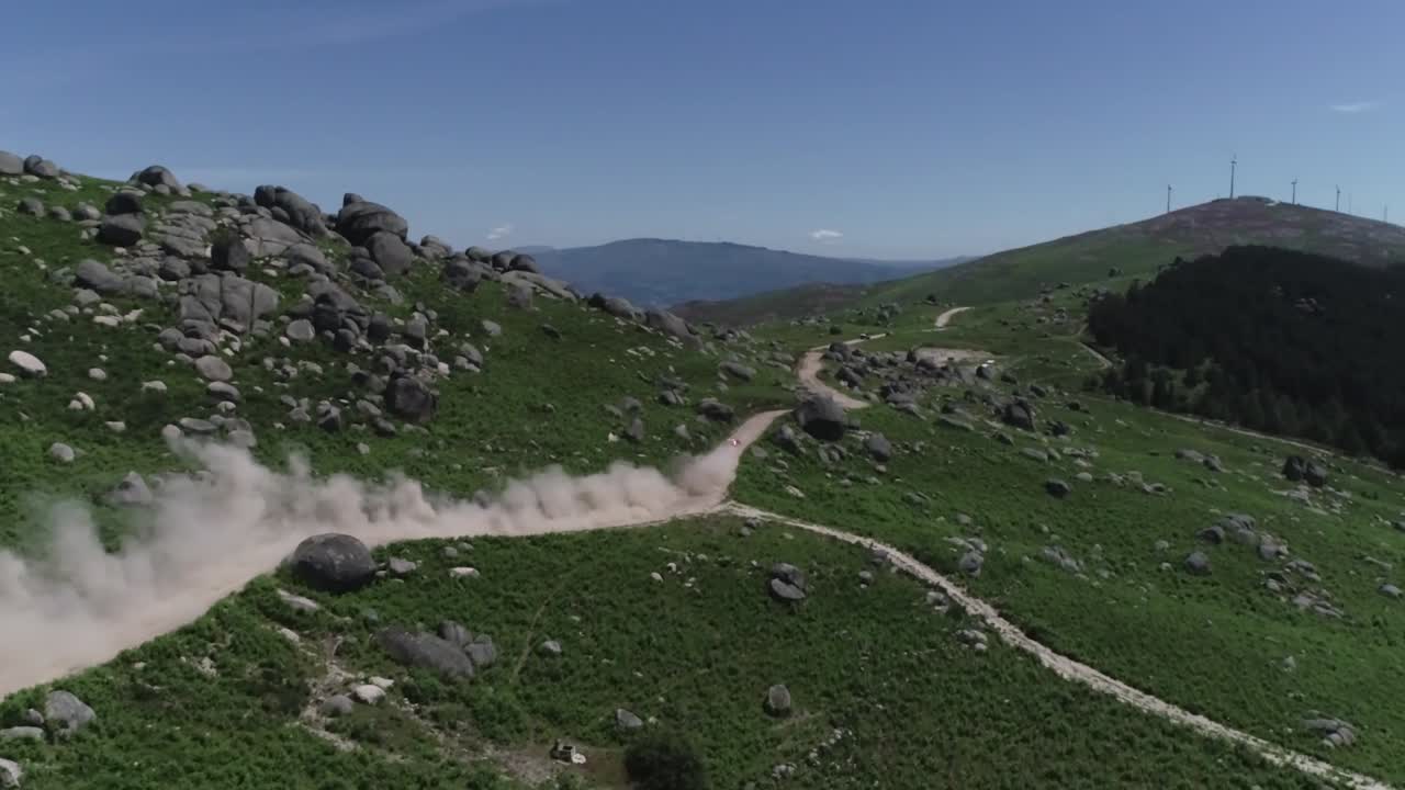 rally car going down a mountain with dust ,shot by drone