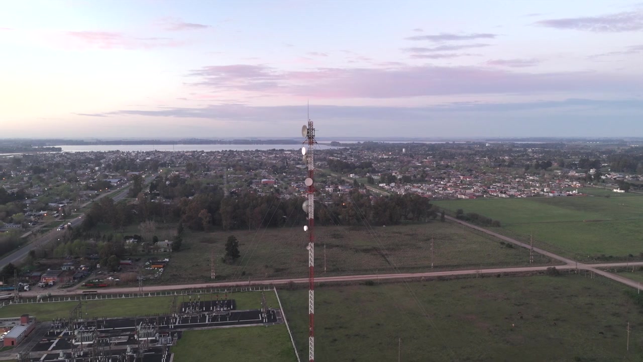 Vista aérea ao amanhecer sobre San Miguel del Monte, na província de Buenos Aires, Argentina, com uma torre de comunicação erguendo-se acima de campos e edifícios sob nuvens em tons pastel