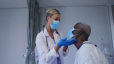 Caucasian-female-doctor-wearing-face-mask-examining-throat-of-african-american-senior-male-patient