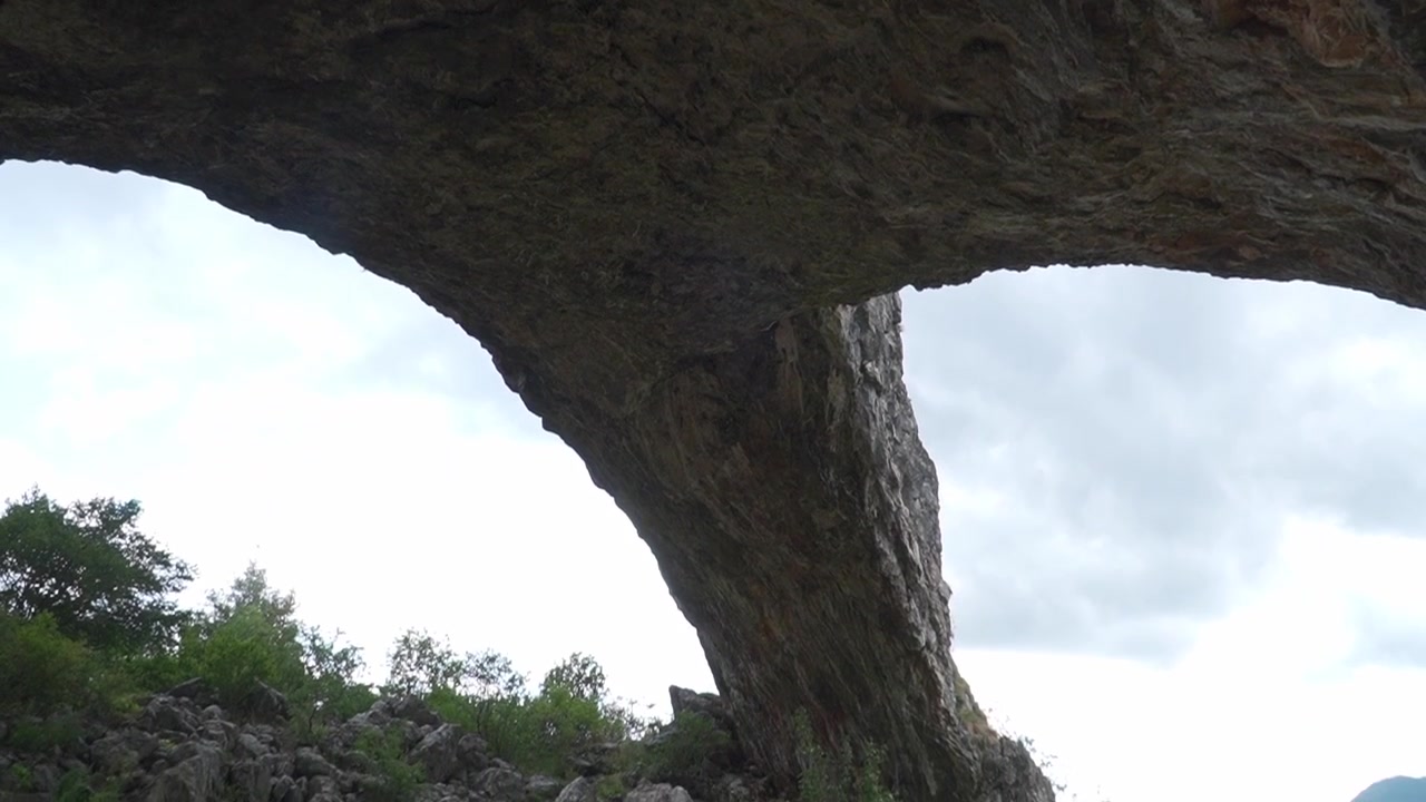 Natural stone arch formation set against a cloudy sky. Rocky mountain landscape showcasing geological features and wilderness textures in a remote outdoor area.