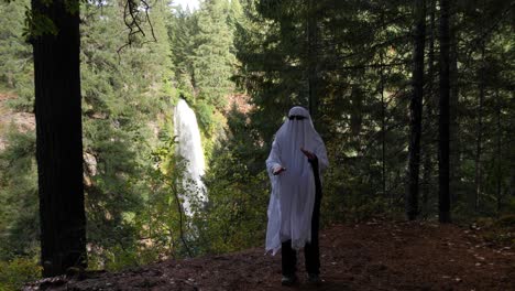 A-person-dressed-as-a-ghost-dances-in-front-of-a-large-waterfall-outlook