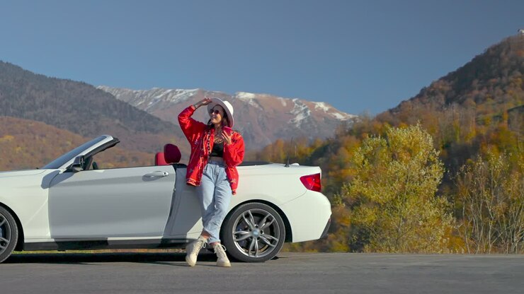 Woman enjoying a scenic road trip in a convertible car amidst autumn foliage
