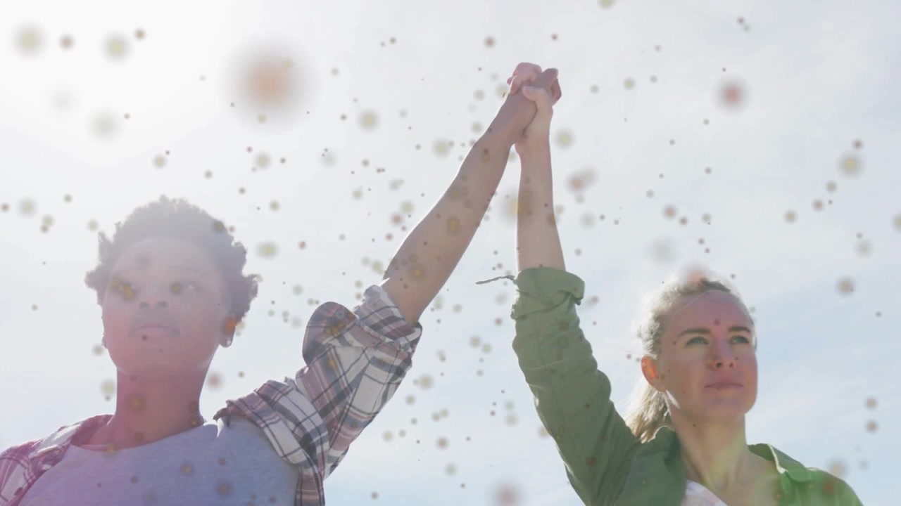 Due donne alzano le mani unite verso il cielo, con un bagliore dell'obiettivo e puntini che attraversano l'inquadratura, a simboleggiare l'unità aziendale.