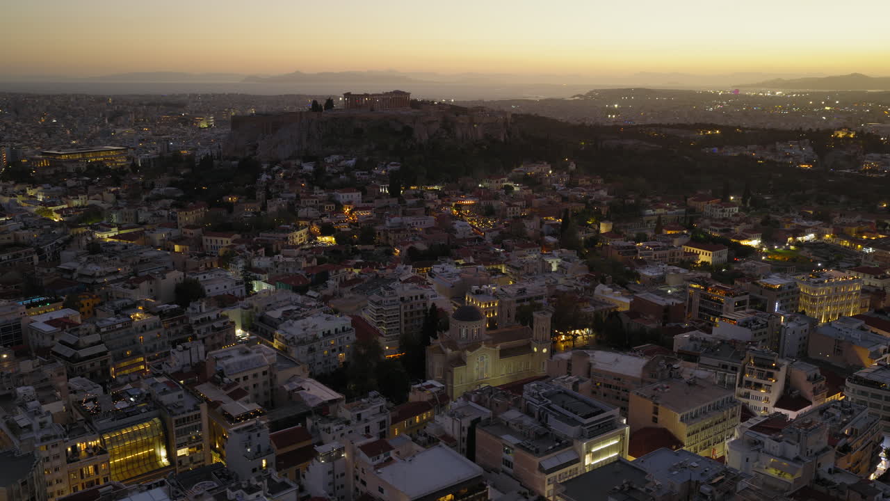 Crepuscolo aereo su Atene con la collina dell'Acropoli che emerge mentre le luci della città iniziano a brillare delicatamente, orbita panoramica