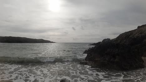 Slow-motion-foaming-ocean-waves-crashing-against-rugged-Welsh-coastline-at-sunrise