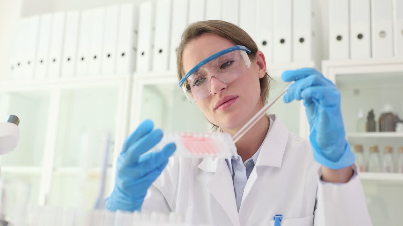 A female scientist in a lab coat and safety glasses working with samples in a laboratory
