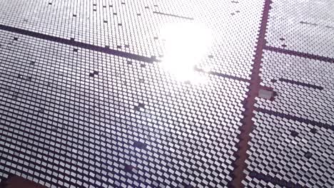 a zoom out and tilt down shot of a solar farm with thousands of heliostat mirrors reflecting sunlight