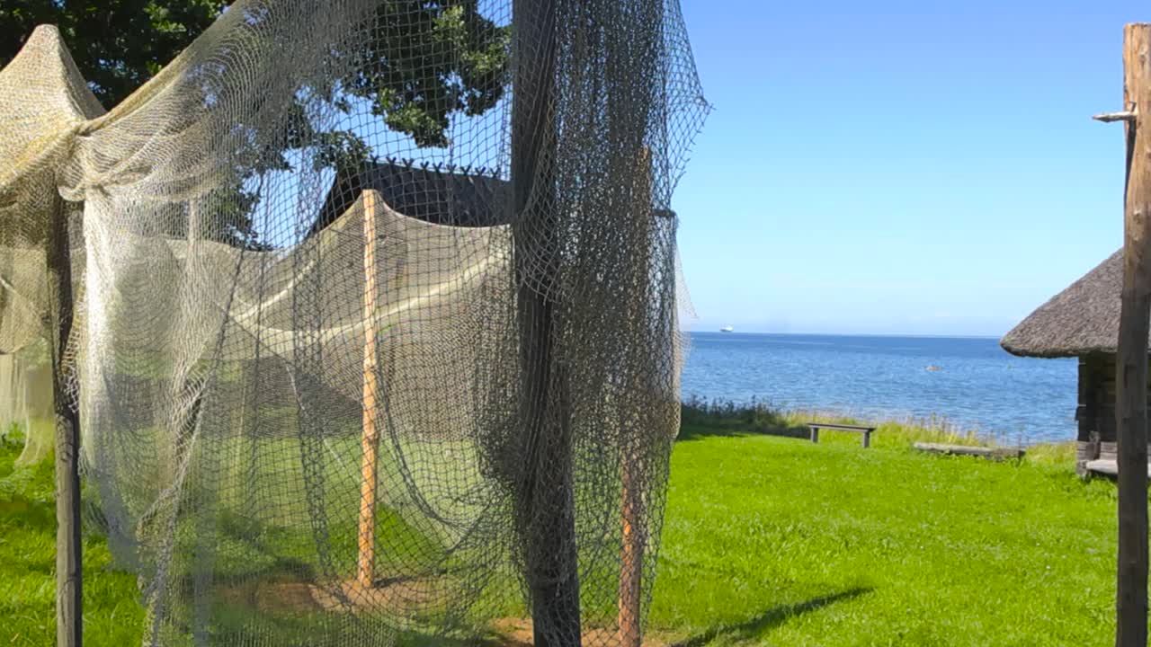 Close up view of old vintage and traditional fishing nets hanging and drying on wooden poles on a shoreline seaside fishing village during a summer sunny day with log cabins with straw roofing visible