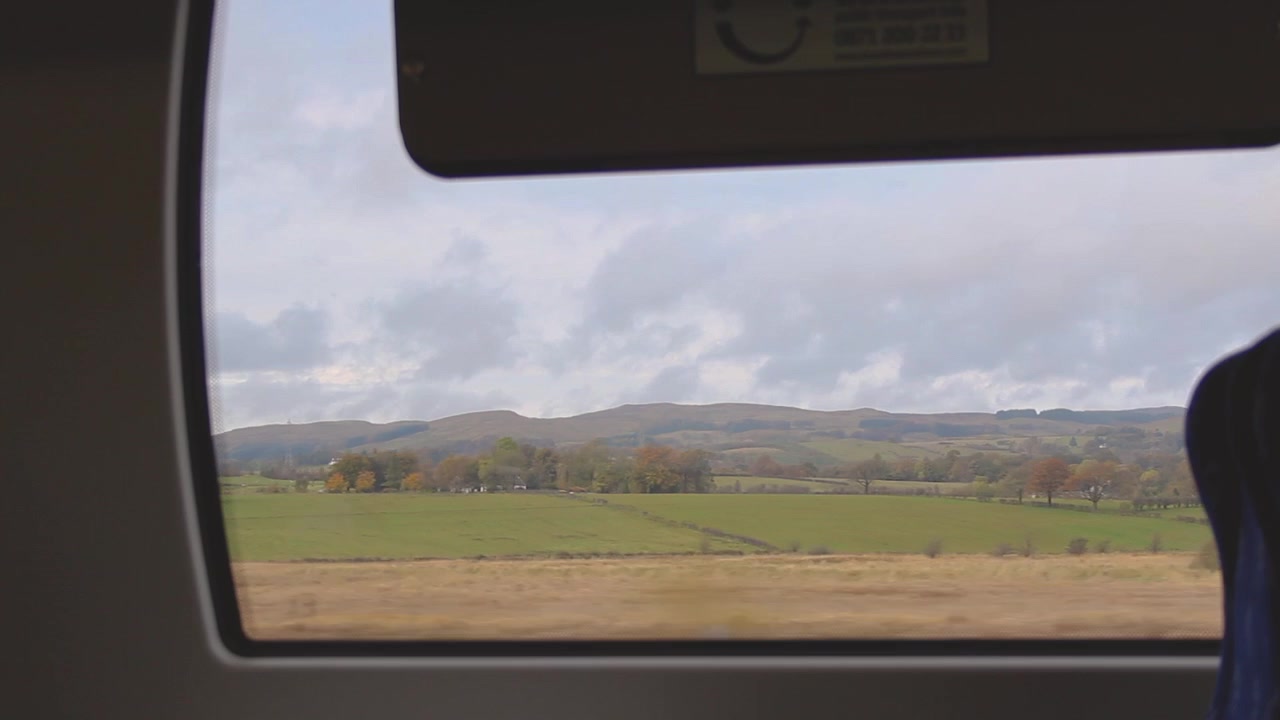 Seeing sunny open wide Scottish autumn landscape with lake and colorful forest through the moving train window.