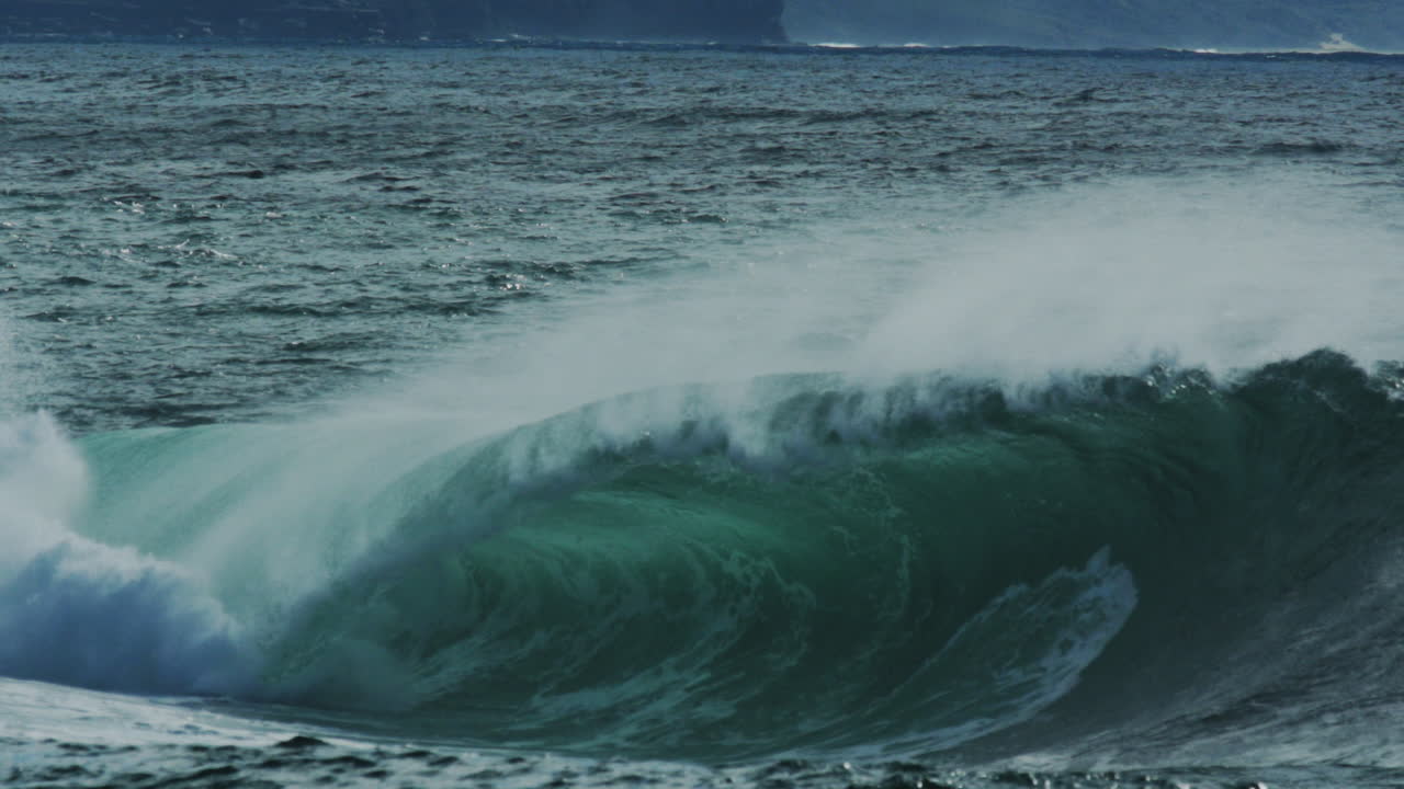 Deep blue swell rolls through frame with rising white spray and light scatter, dramatic ocean energy