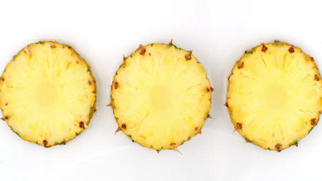 3 pineapples lie on a white in the background in slow motion falling water splashes.