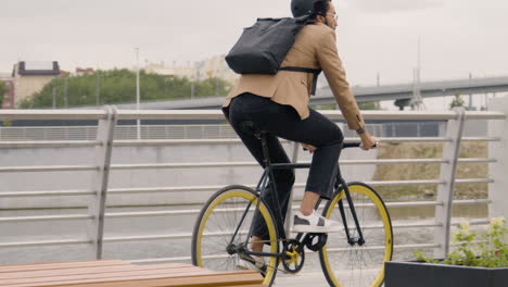 joven americano vestido con ropa formal con casco y mochila yendo a trabajar en bicicleta