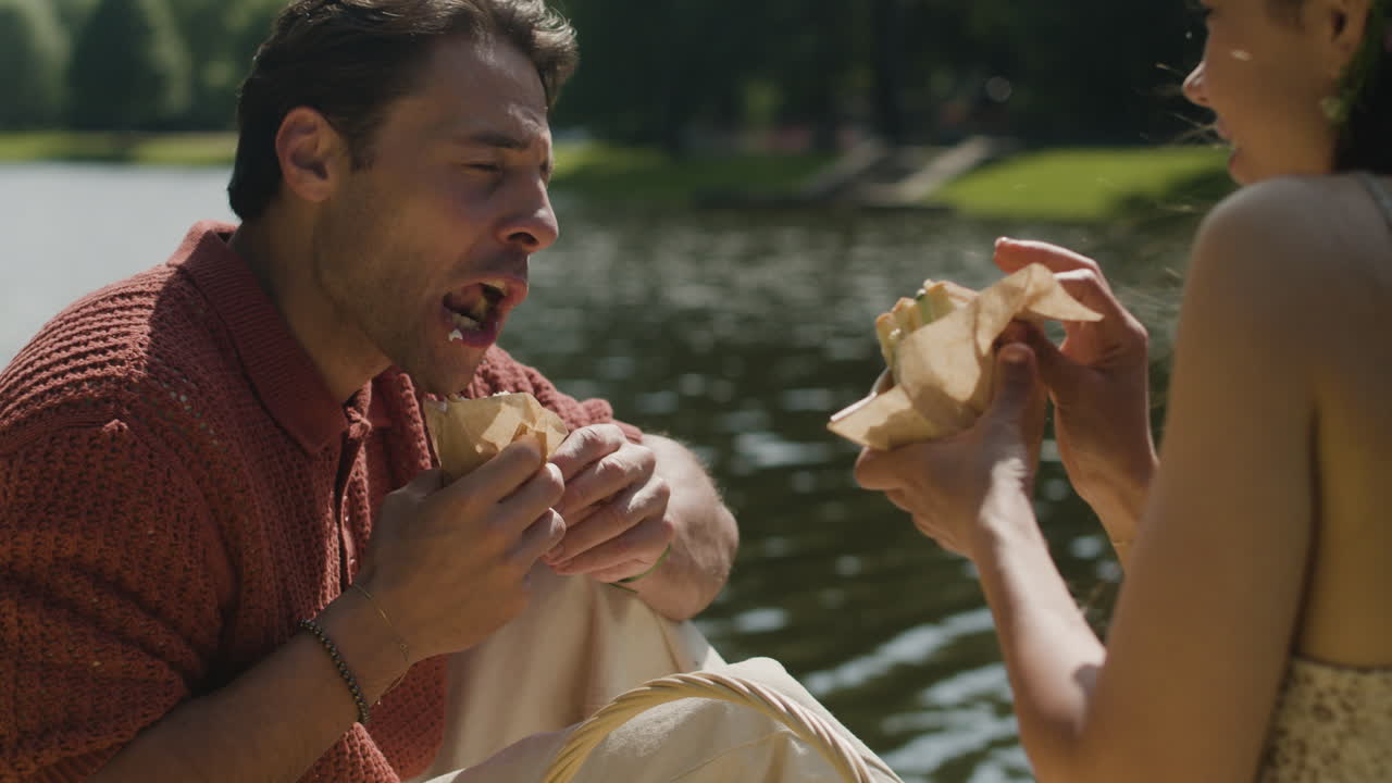 Couple eating sandwiches by the lake