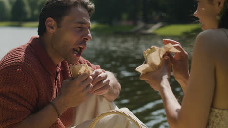 couple eating sandwiches by the lake